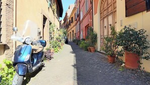 A narrow cobblestone street lined with buildings, a parked scooter, and potted plants. - Luxury Maison Colosseum, like a resident (Roma)