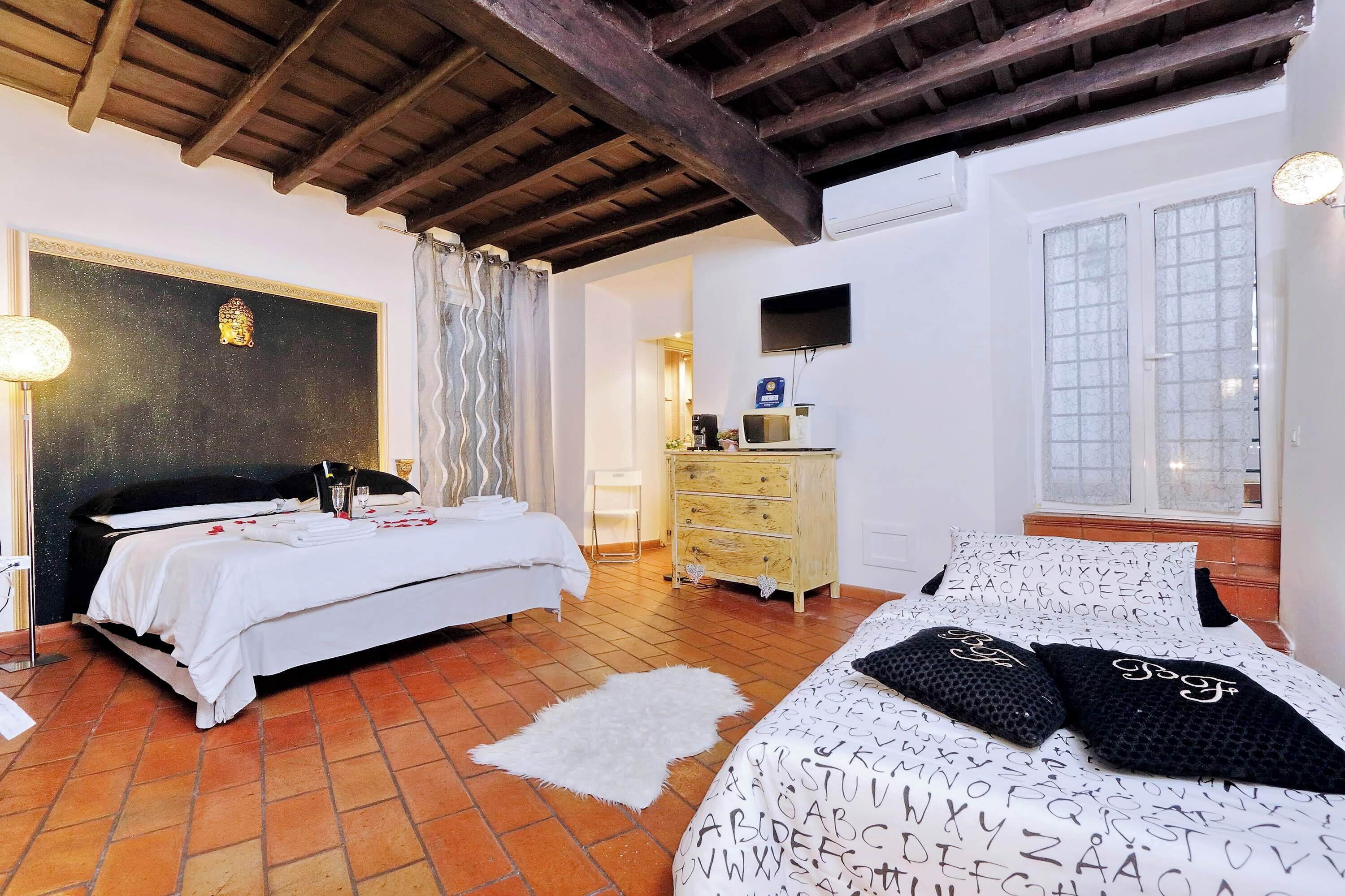 Un dormitorio con dos camas, techo de madera, cómoda blanca, televisor y ventana con vidrio esmerilado.