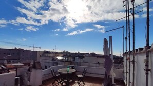 A rooftop terrace with a round table and chairs, surrounded by potted plants and a statue. - Luxury Maison Colosseum, like a resident (Roma)