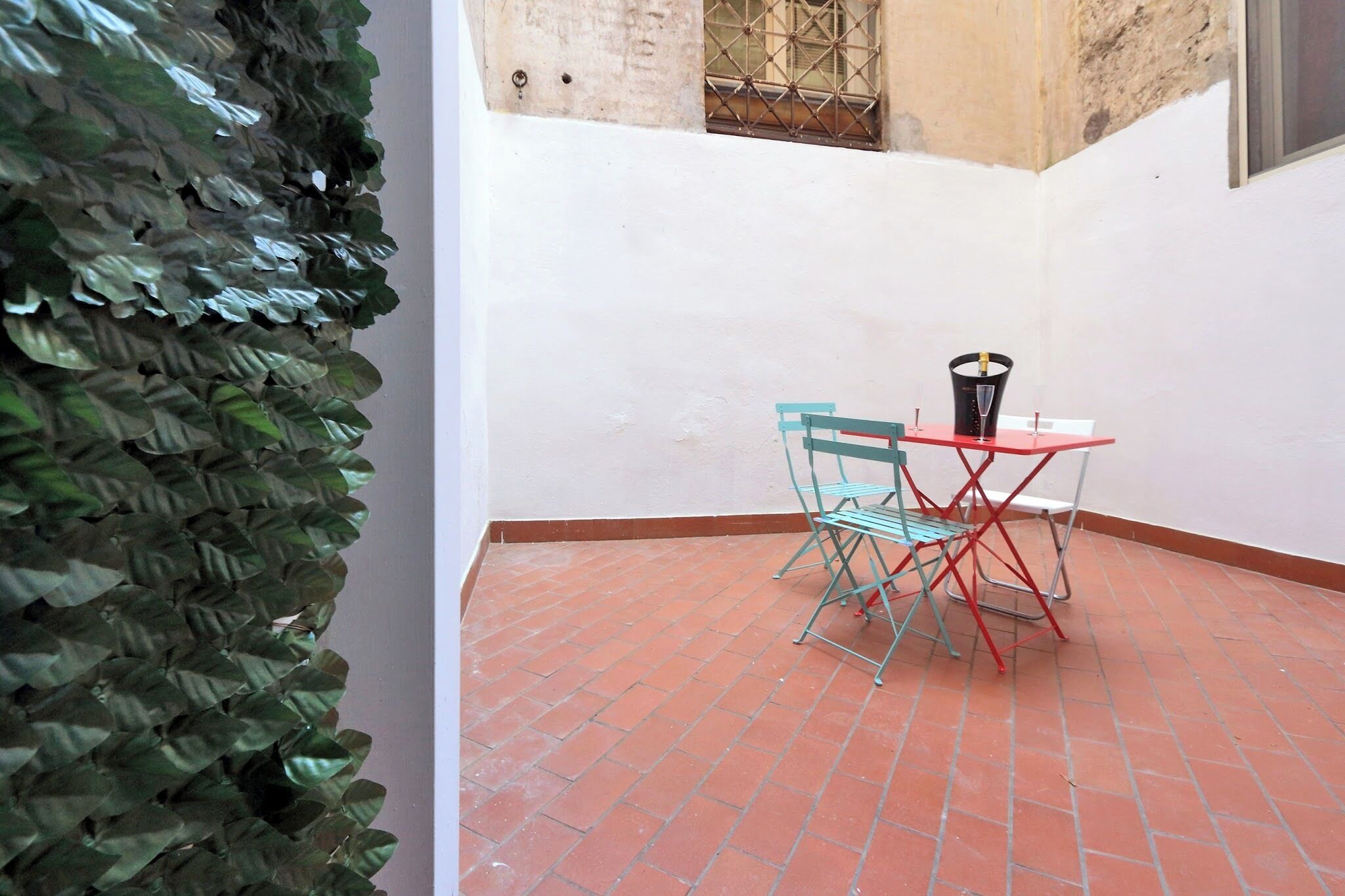 A patio with a tiled floor, a table with two chairs, and a decorative plant.