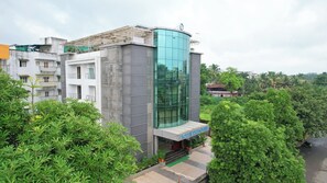A modern hotel with a glass facade, surrounded by lush greenery. - Hotel The Seven (Silvassa)