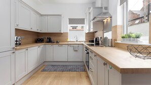 Una cucina moderna con mobili bianchi, un piano di lavoro in legno, un forno integrato e una finestra con vista sull'esterno.