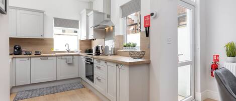 A modern kitchen with white cabinets, a built-in oven, and a window overlooking a brick building.