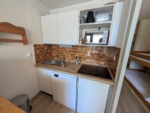 Una kitchenette compacta con lavavajillas integrado, microondas y pileta con salpicadero marrón.