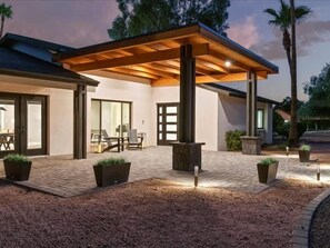 Una casa moderna con patio coperto, posti a sedere all'aperto e un braciere.