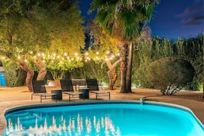 Una piscina con lettini e luci decorative, circondata da alberi e vegetazione.