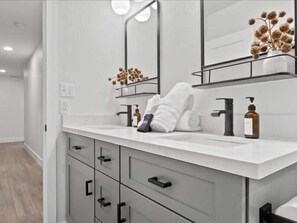 Un baño moderno con tocador blanco, un espejo grande y un perchero para toallas.