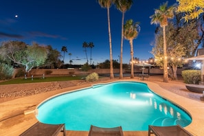 Una piscina de borde curvo, rodeada de palmeras y un patio con mobiliario exterior.