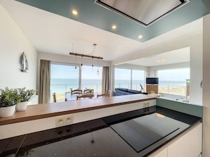 A modern kitchen with a large island, a dining area with a view of the sea, and a living area with a sofa and TV. - Flat Sunset - amazing seaview (De Panne)
