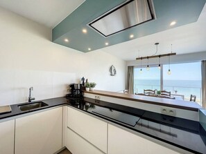A modern kitchen with a black countertop, white cabinets, and a view of the sea through large windows. - Flat Sunset - amazing seaview (De Panne)