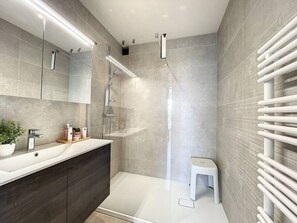 A modern bathroom with a glass-enclosed shower, a vanity with a sink, and a towel rack. - Flat Sunset - amazing seaview (De Panne)