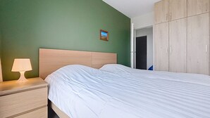 A bedroom with a bed, a nightstand with a lamp, and a wardrobe. - Flat Sunset - amazing seaview (De Panne)