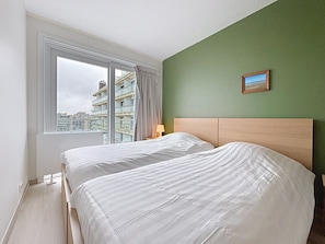 A hotel room with a large bed, a view of the city through a window, and a green wall. - Flat Sunset - amazing seaview (De Panne)
