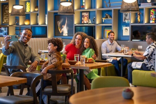 A restaurant with multiple tables and chairs, a variety of wall decorations, and hanging lamps. - Aloft Orlando Lake Nona (Orlando)
