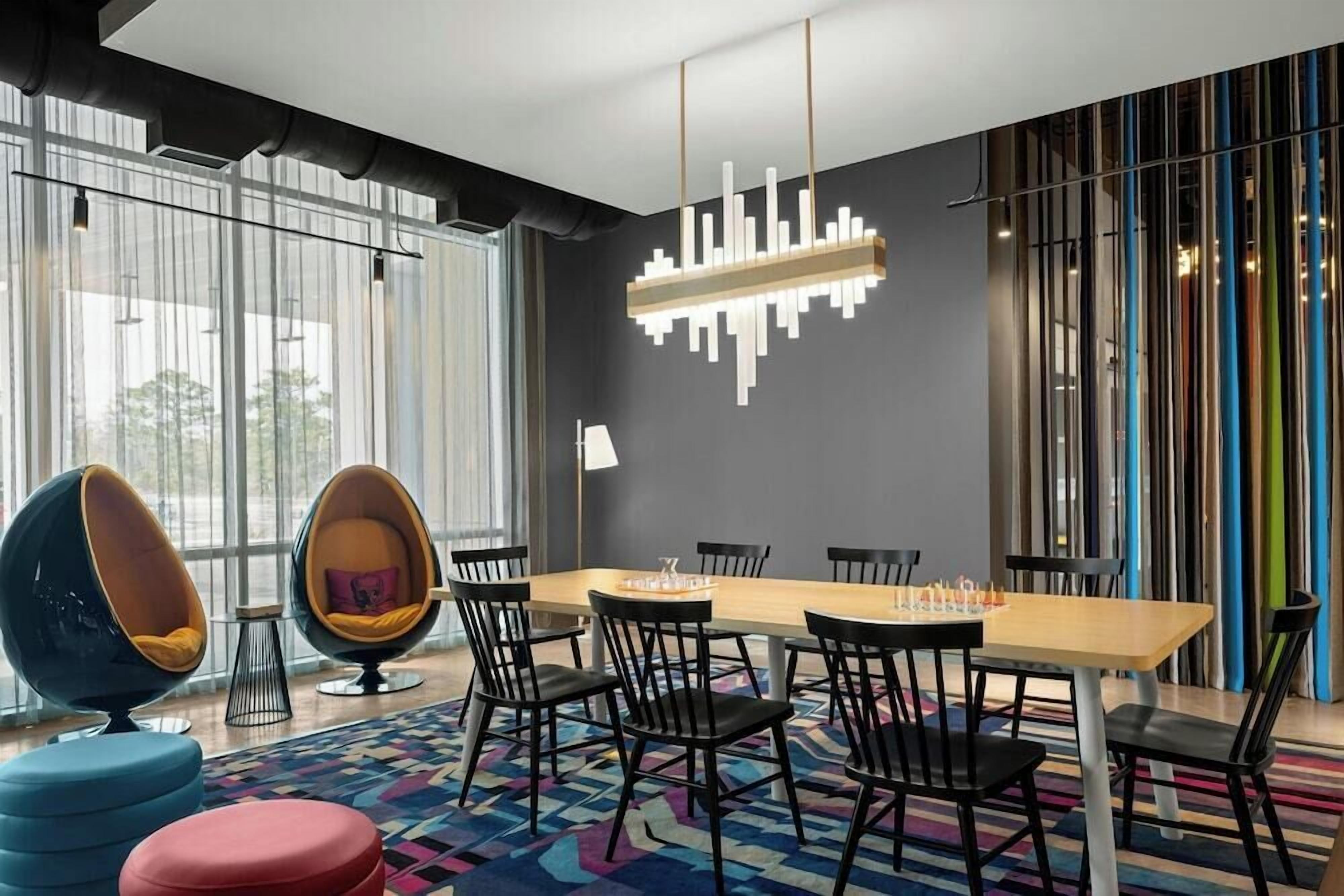 Un espace repas moderne avec une longue table, des chaises noires et des coussins colorés.