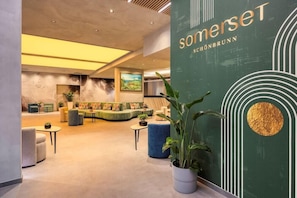 Een moderne hotel lobby met een groene wand, zithoeken en een grote plant.