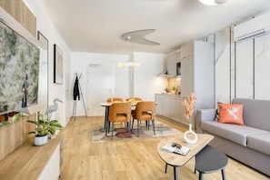 Een moderne woonkamer met een bank, een eettafel met stoelen, een salontafel en een keuken op de achtergrond.