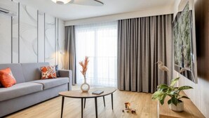 A modern living room with a sofa, a coffee table, a plant, and a large window with curtains. - Somerset Schoenbrunn Vienna (Vienna)