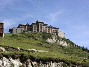 Um edifício grande, com várias andares e fachada de pedra, localizado numa encosta gramada.