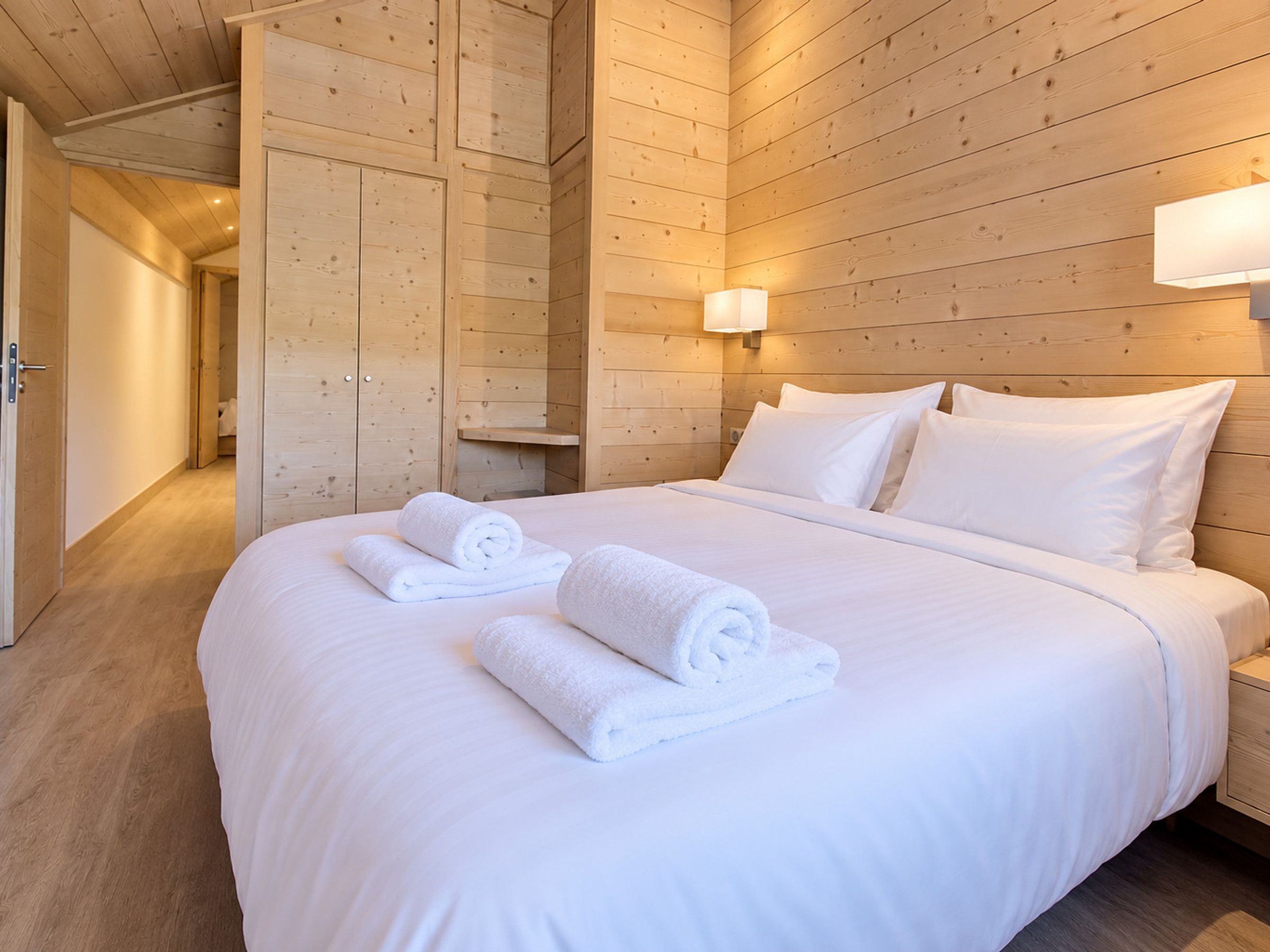 A hotel room with a wooden ceiling, a bed with white linens, and a nightstand with a lamp.