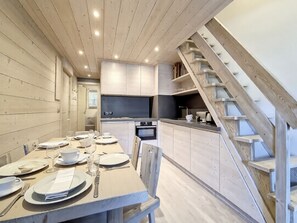 A modern kitchen with wooden cabinets, a dining table set for four, and a staircase leading to an upper level.