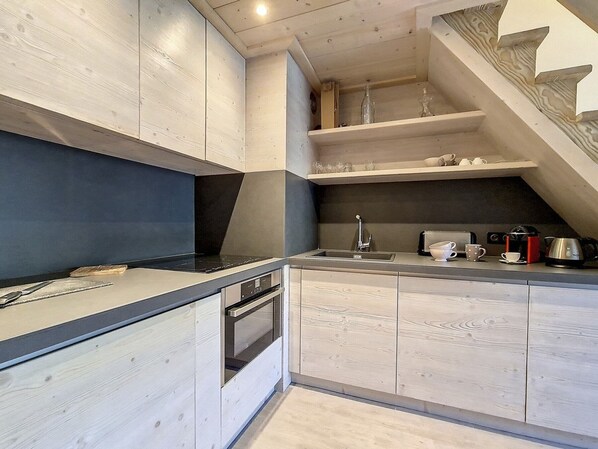 A modern kitchen with wooden cabinetry, a built-in oven, a sink, and a coffee maker.