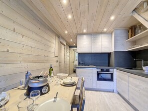 Uma cozinha moderna com paredes de madeira, área de refeições com mesa posta para dois e eletrodomésticos embutidos.