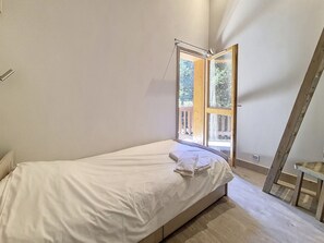 Quarto com uma cama de solteiro, janela com vista para um deck de madeira e teto inclinado.
