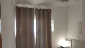 A bedroom with a bed, a nightstand, a ceiling fan, and a window with curtains.