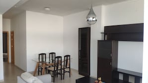 A modern living room with a sofa, dining table, chairs, a TV stand, and a pendant light.