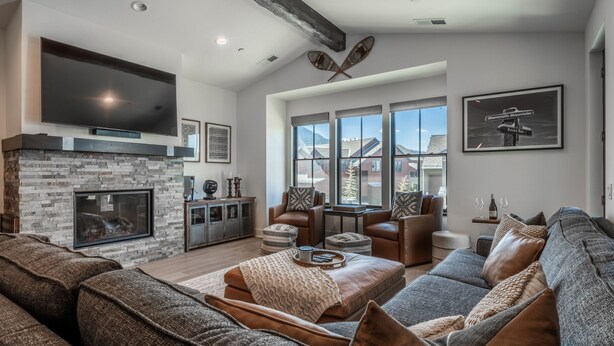 Ein geräumiges Wohnzimmer mit Kamin aus Stein, Ledersofas und großen Fenstern mit Bergblick.