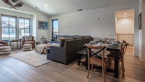 Ein geräumiges Wohnzimmer mit grauem Sofa, einem Esstisch für vier Personen und einem großen Fenster mit Blick nach draußen.