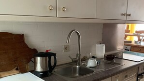 Eine Küche mit weißen Schränken, einer Edelstahl-Spüle, einem Wasserkocher und einer Kaffeemaschine.