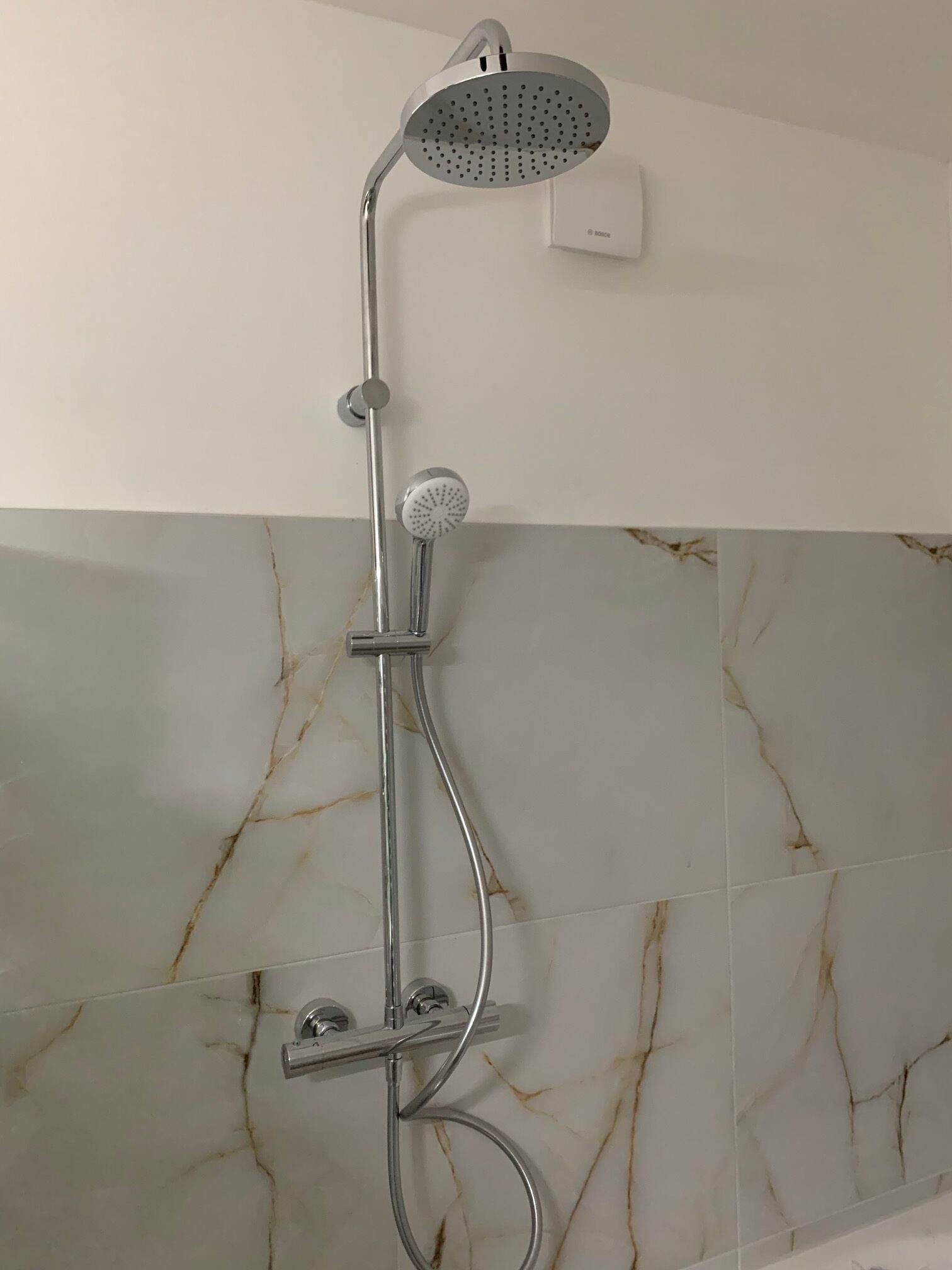Eine Dusche mit verstellbarem Duschkopf, an einer Wand mit Marmorfliesen.