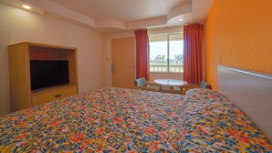 Quarto de hotel com cama, televisão, uma mesinha e janela com cortinas.