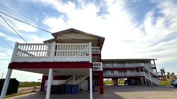 A two-story building with a balcony on the upper level, a staircase leading to the upper floor, and a parking area in front.