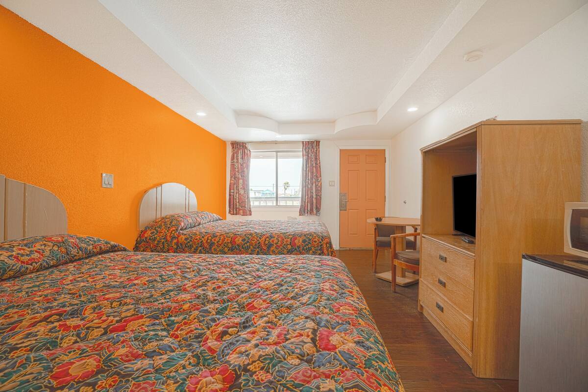 A bedroom with two beds, a wooden wardrobe, a television, and a window with curtains.