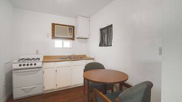 Cocina compacta con estufa a gas, armarios blancos, encimera de madera y una mesa de comedor con sillas.