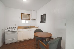 A compact kitchen with a gas stove, white cabinets, a wooden countertop, and a dining table with chairs. - Budget Inn By Oyo Corpus Christi Beach (Portland)