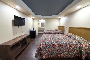 A bedroom with a bed, a TV mounted on the wall, a wooden bench, and a mirror above the sink. - Budget Inn By Oyo Corpus Christi Beach (Portland)