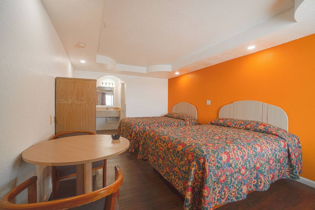 A bedroom with two beds, a wooden table, and a small kitchenette.