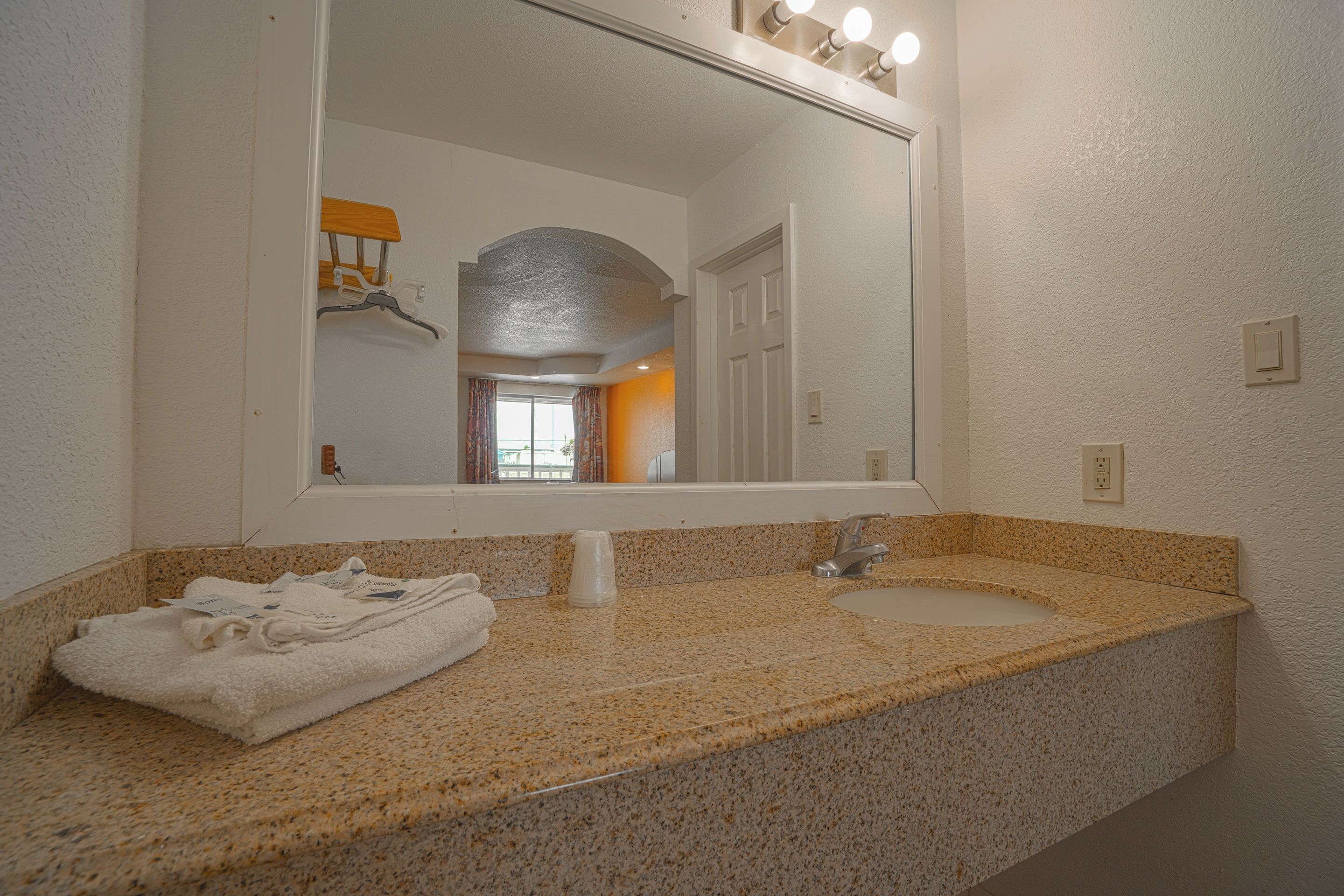 Une salle de bain avec un comptoir en granit, un lavabo, un miroir et un porte-serviettes.