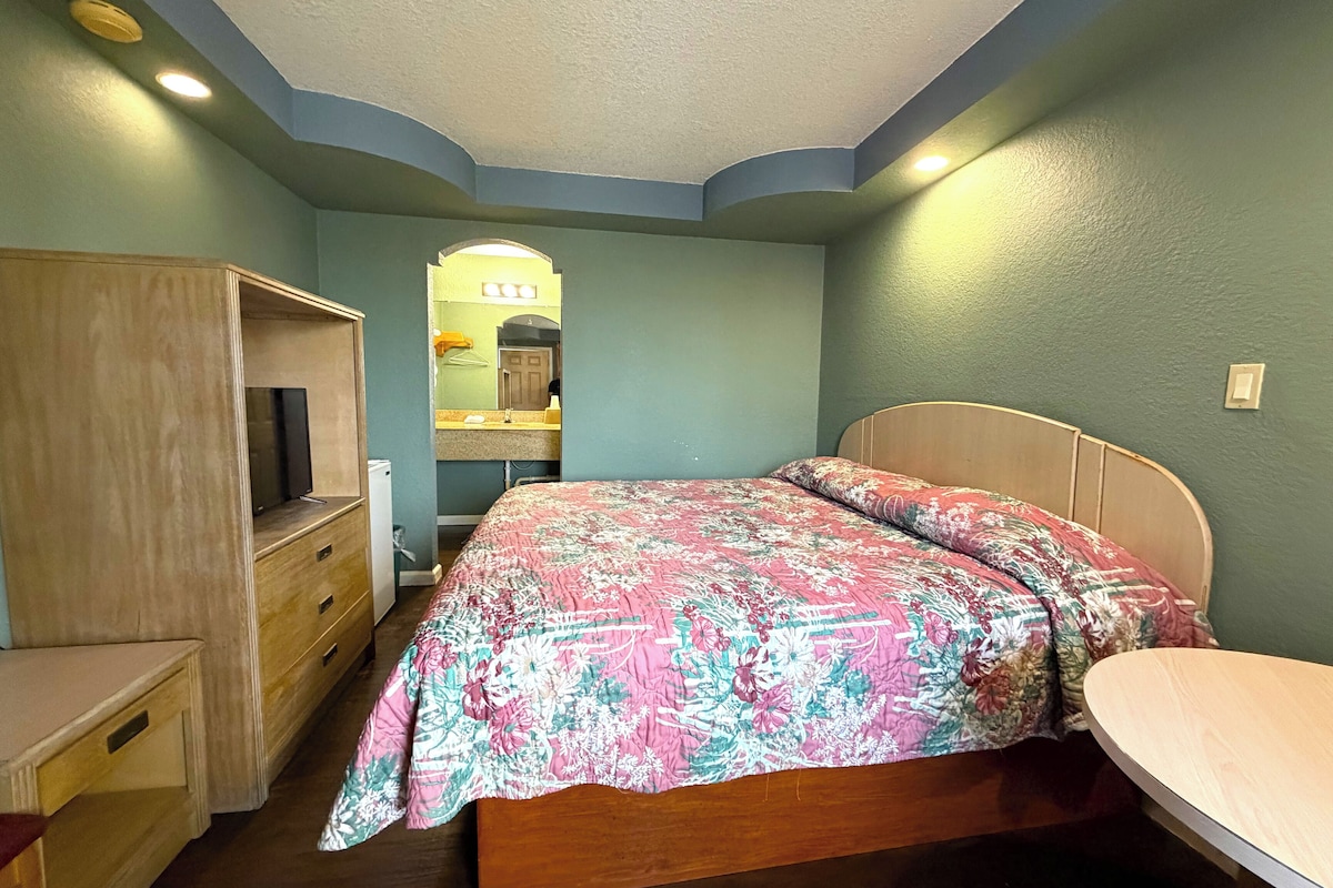 A bedroom with a bed, a wooden dresser, a desk, and a mirror.