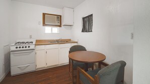 Cozinha compacta com fogão a gás, armários brancos, bancada de madeira e mesa de jantar com cadeiras.
