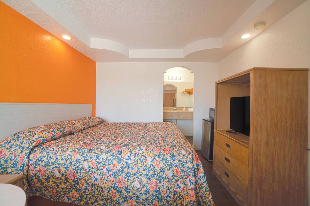 A bedroom with a bed, a TV, and a wooden wardrobe.