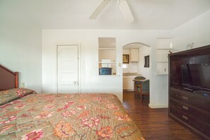 A bedroom with a bed, a dresser, a television, and a kitchen area visible through an archway. - Budget Inn By Oyo Corpus Christi Beach (Portland)
