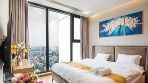 Ein modernes Hotelzimmer mit einem großen Bett, einem Schreibtisch mit Computer, einer Blumenvase und Blick auf die Stadt.
