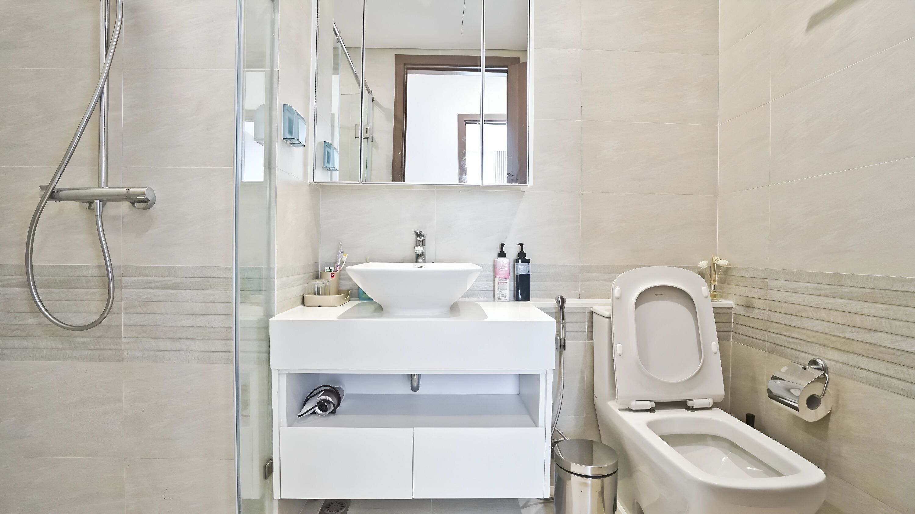 Une salle de bain moderne avec une douche à parois de verre, un lavabo blanc avec un receveur, des toilettes et un miroir au-dessus du lavabo.