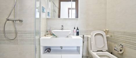 Une salle de bain moderne avec une douche à parois de verre, un lavabo blanc avec un receveur, des toilettes et un miroir au-dessus du lavabo.