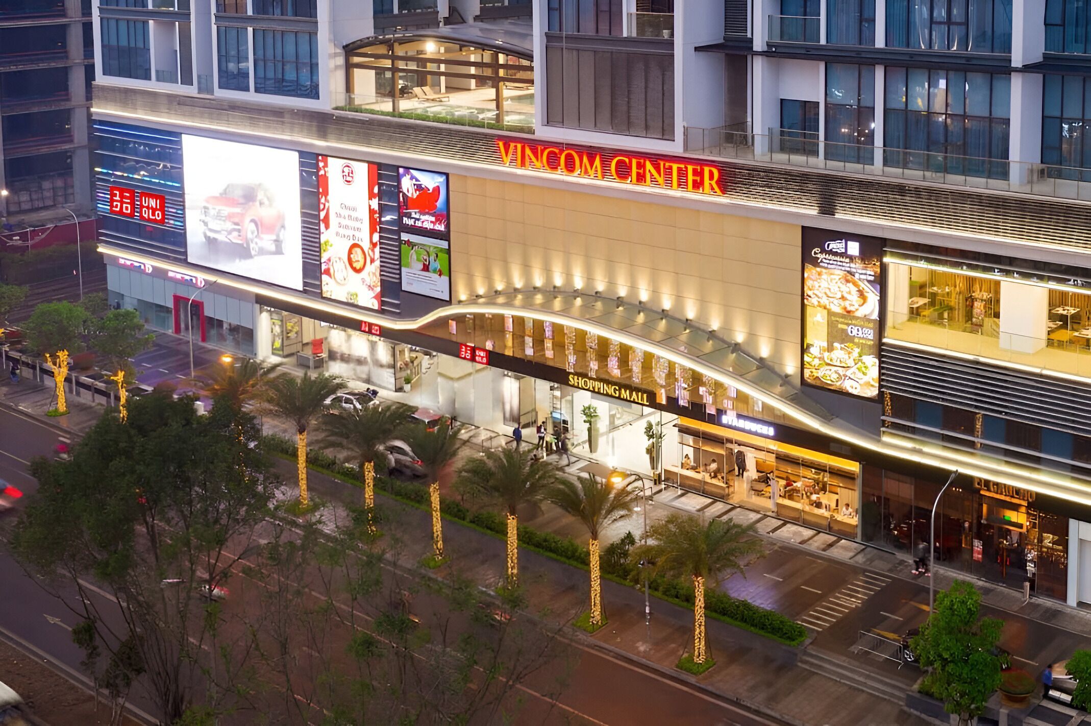 A modern shopping mall with a prominent Vincom Center sign, multiple large digital billboards, and a variety of retail stores.